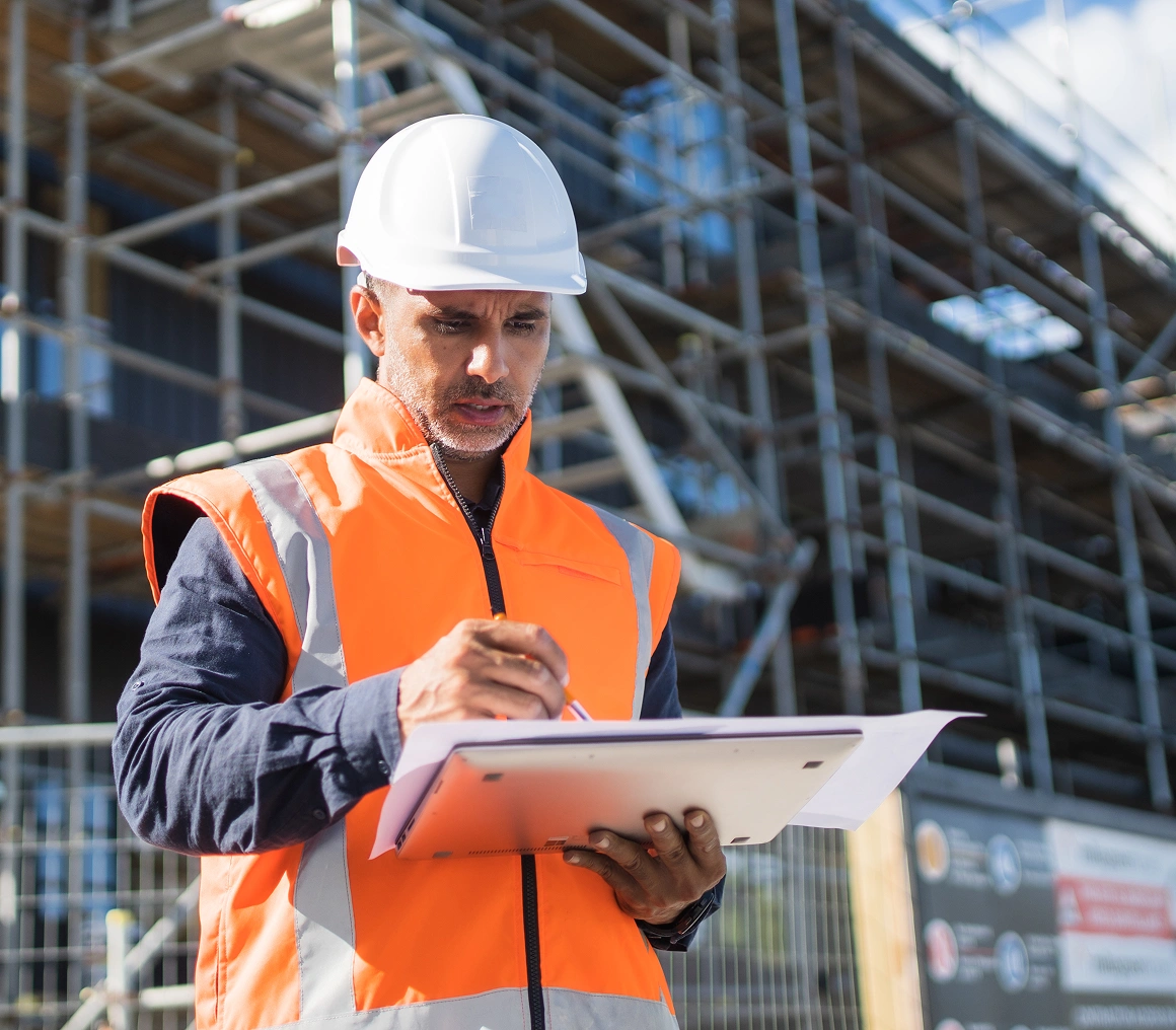 Construction worker writing on clipboard outside.